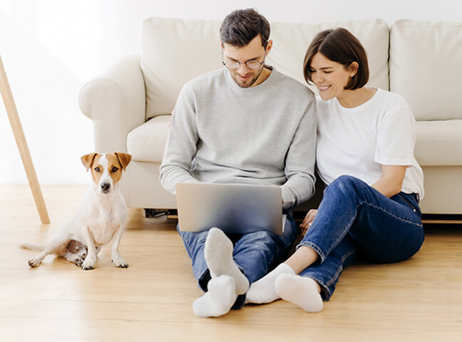 Smiling Couple Examine Their Family Health Plan Options On A Laptop With Their Dog