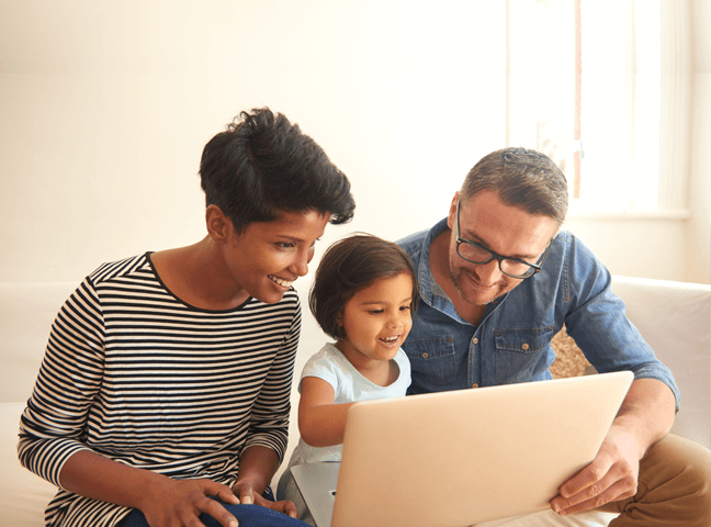 Smiling Couple Examine Their Family Health Plan Options On A Laptop With Their Daughter