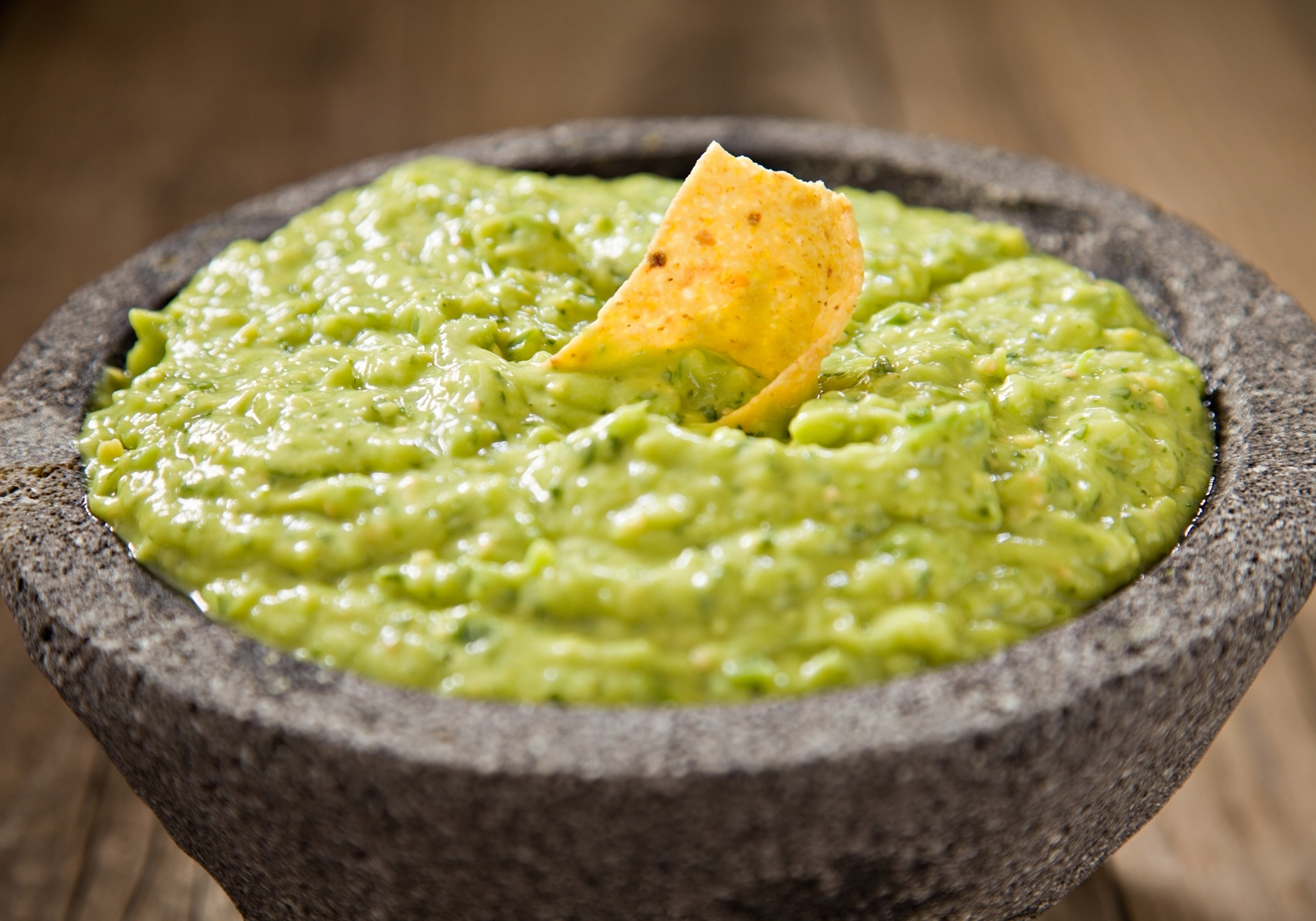 Photo: Tomatillo guacamole and tortilla chip in a stone bowl.