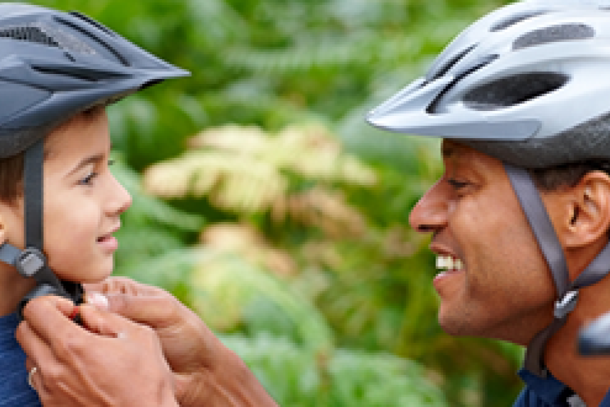 A man helps buckle his young son's bicycle helmet