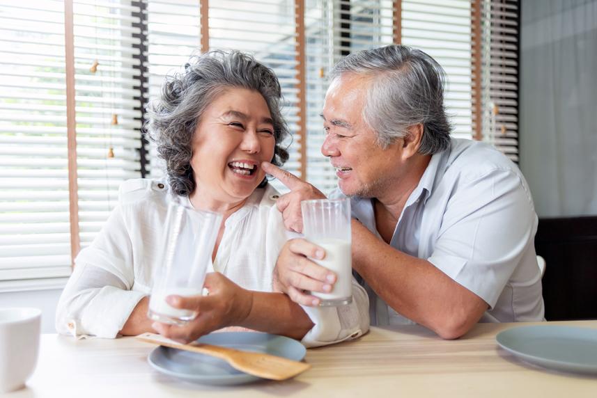 A smiling couple sitting at a table, each holding a glass of milk