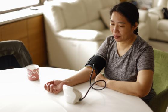 A woman takes her blood pressure at a table in her home.