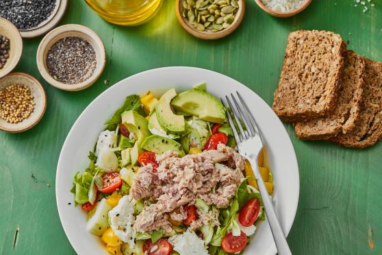 A close-up photo of a salad topped with avocado, shredded tuna, cherry tomatoes.