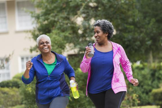 Two middle-aged women are exercising by walking together. They are both holding water bottles and pumping their arms as they walk.