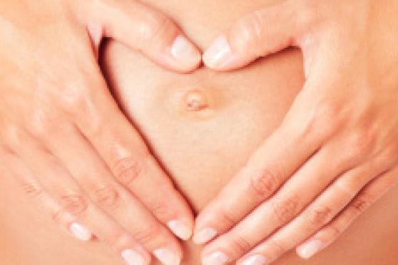 Photo: Woman holding hands in the shape of a heart over her stomach