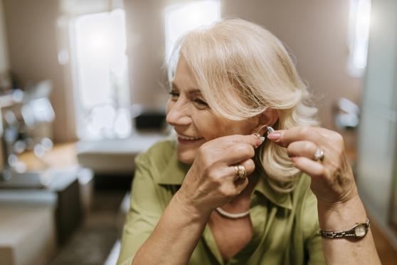 elderly woman putting on hearing aid