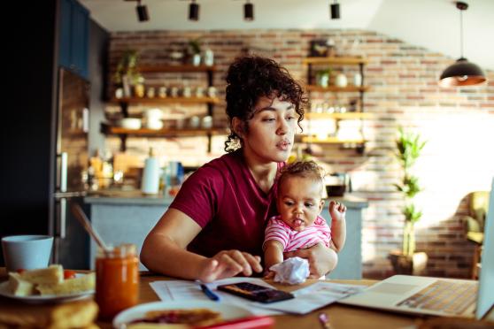 Woman holding baby using a laptop at a cafe.