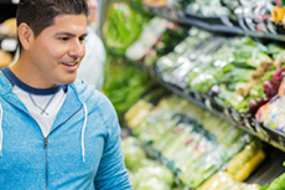 A young man in a sky blue zip-up hoodie peruses the options in the produce section of a grocery store.