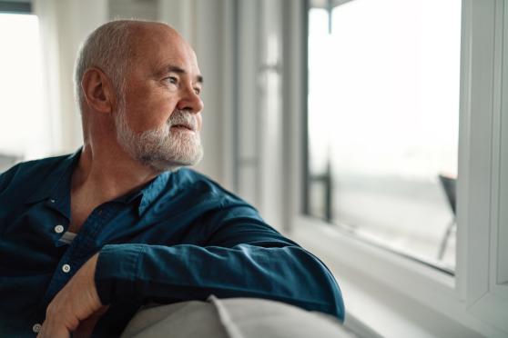 A man looks pensively out the window after receiving a prostate cancer diagnosis.