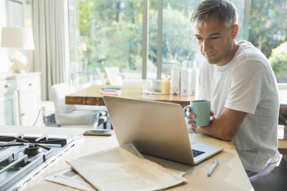 A man researches his prostate cancer treatment options on a laptop while sitting at his kitchen counter.