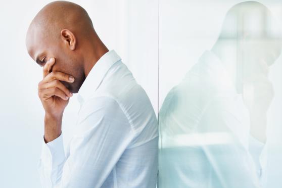 Photo: Man leaning against a wall having a thoughtful moment.