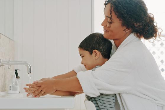 A mother helping her child wash thier hands. 